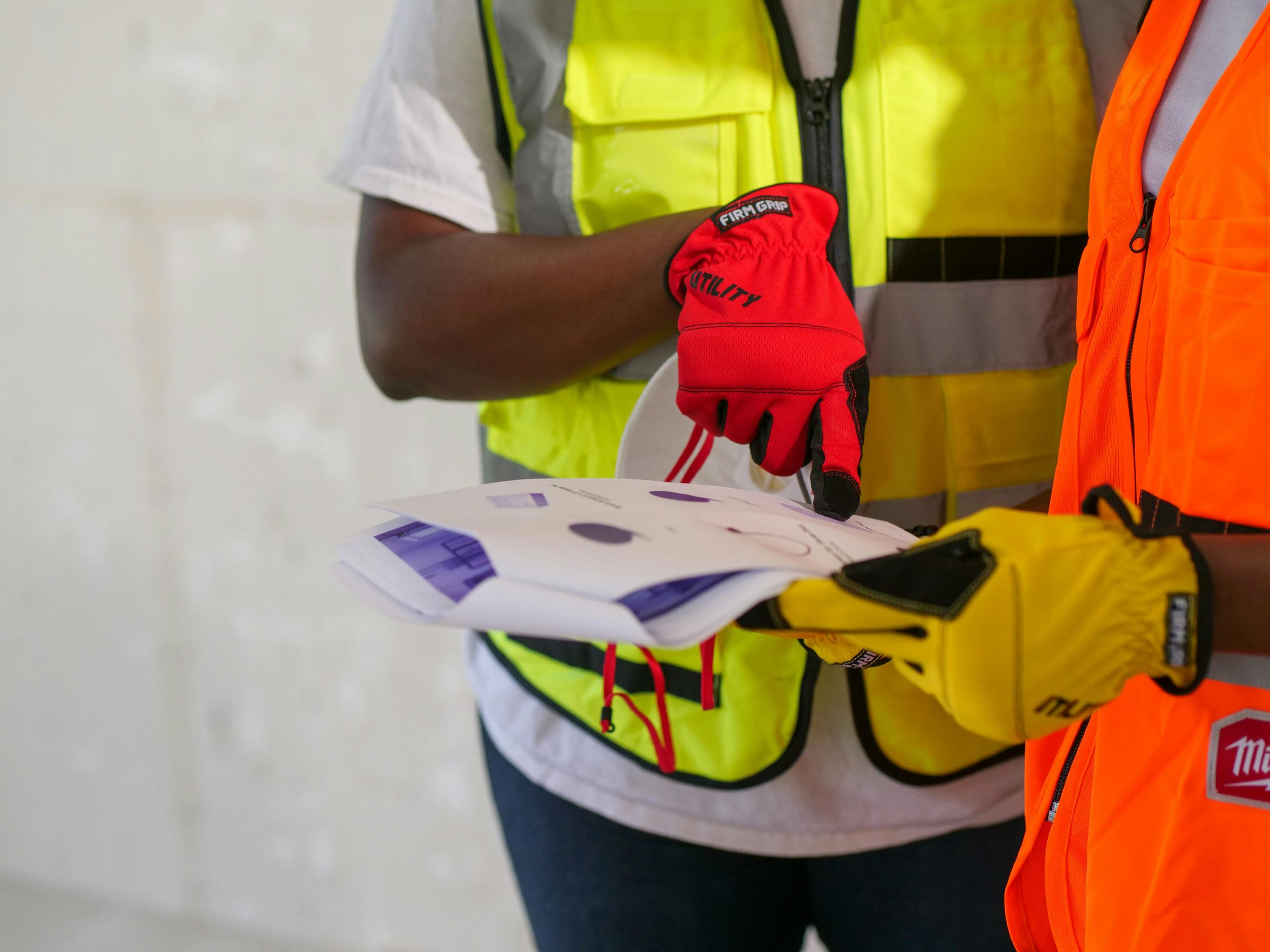 Close-up of construction workers with safety gear reviewing printed documents.